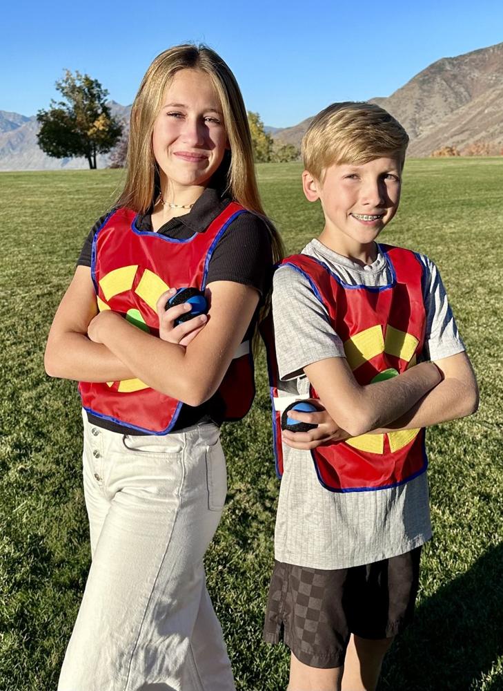 A teenage girl and a boy in red target vests stand back to back with arms crossed, holding sticky balls