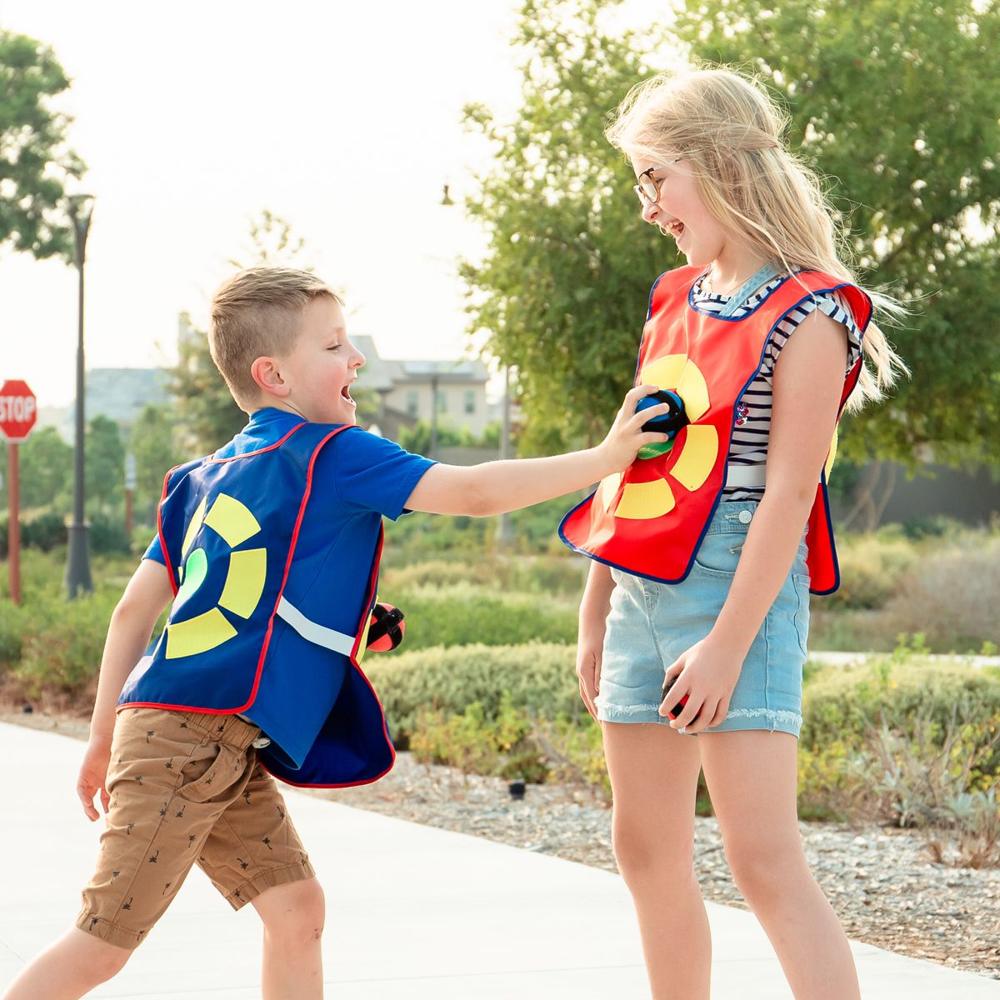 A laughing boy in a blue vest presses a sticky ball onto his sister's red target vest