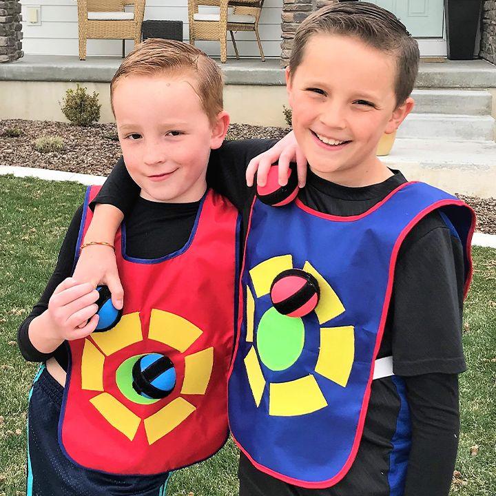 Two boys smiling in red and blue vests with balls stuck to their targets